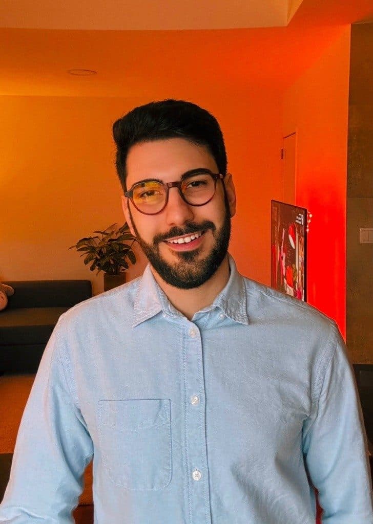 Gabriel Espinheira, founder of SharpHaw, in a light-blue shirt in a warm orange-lit room.
