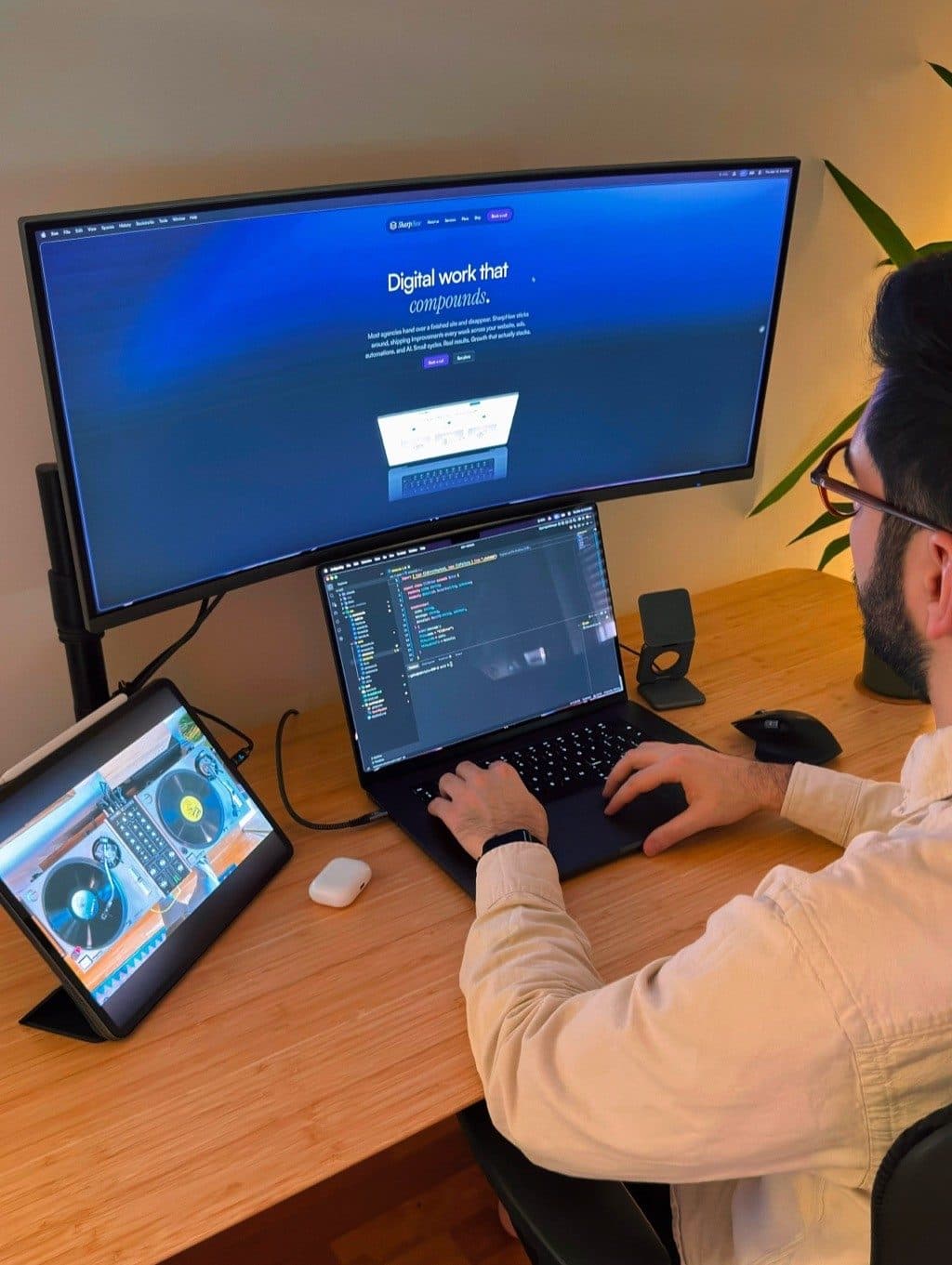 The SharpHaw desk: an ultrawide monitor showing the SharpHaw homepage above a laptop mid-code.