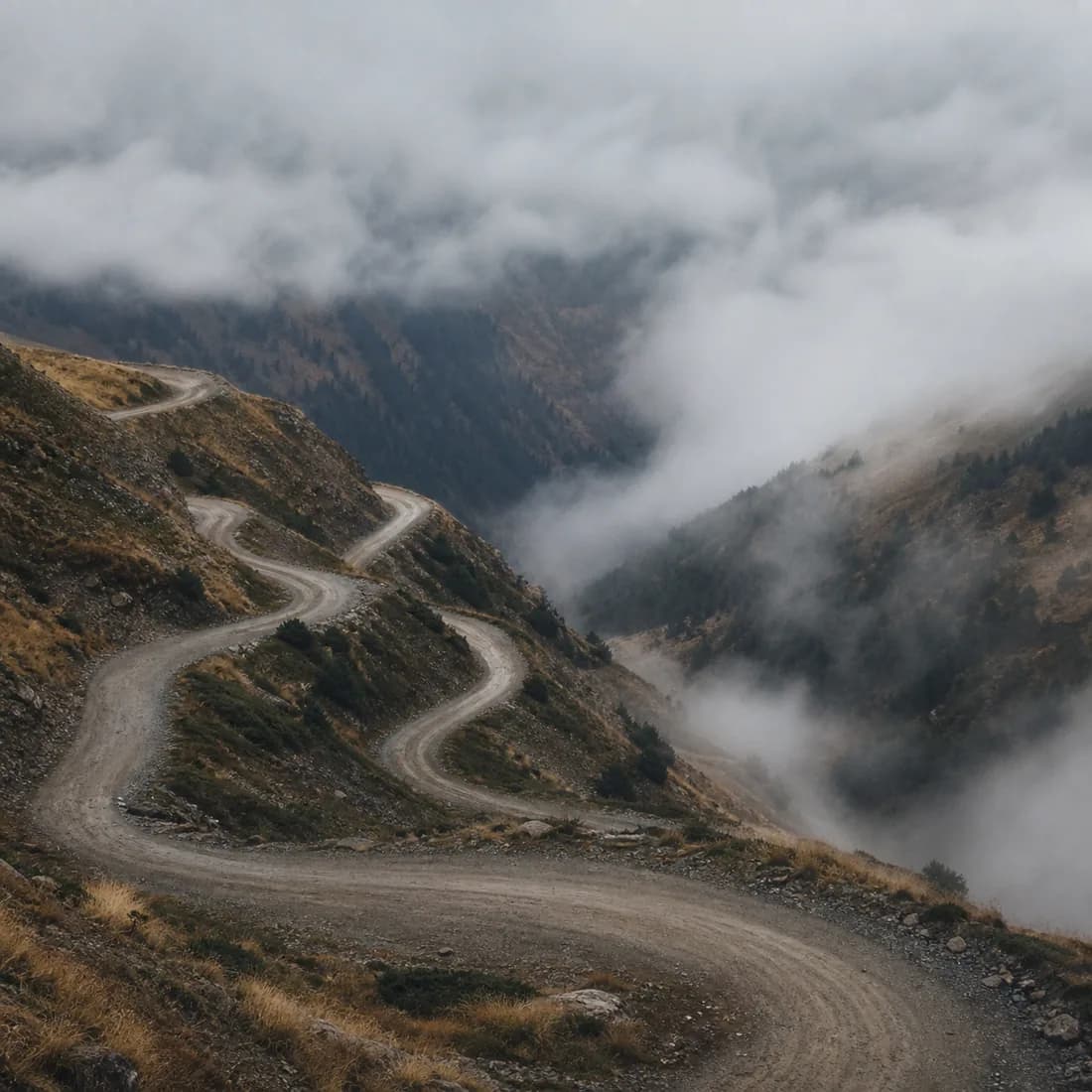 An empty mountain road switching back into cloud, no cars and no signs, mist filling the valley below