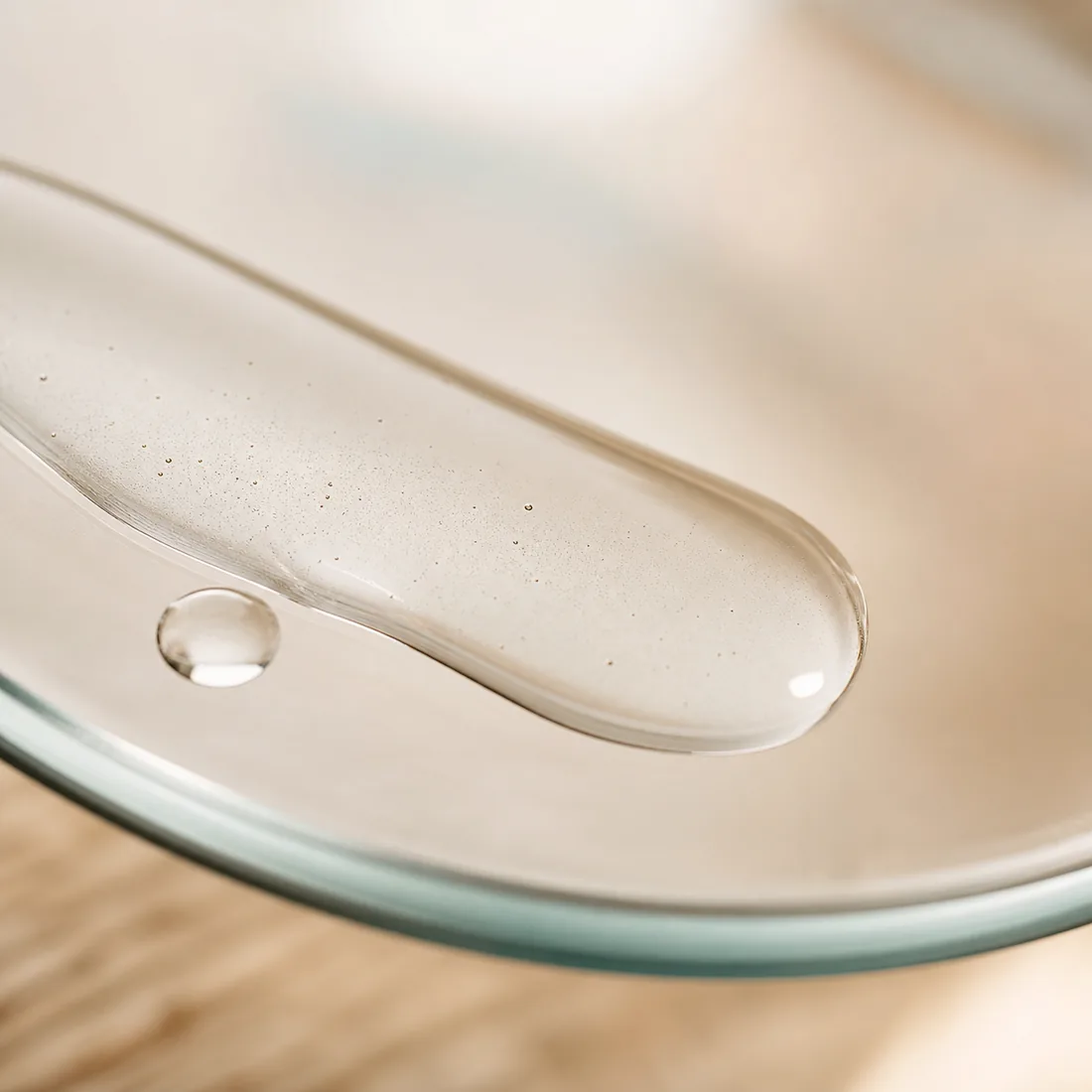 A macro of clear serum on clean glass, cream background, one soft highlight