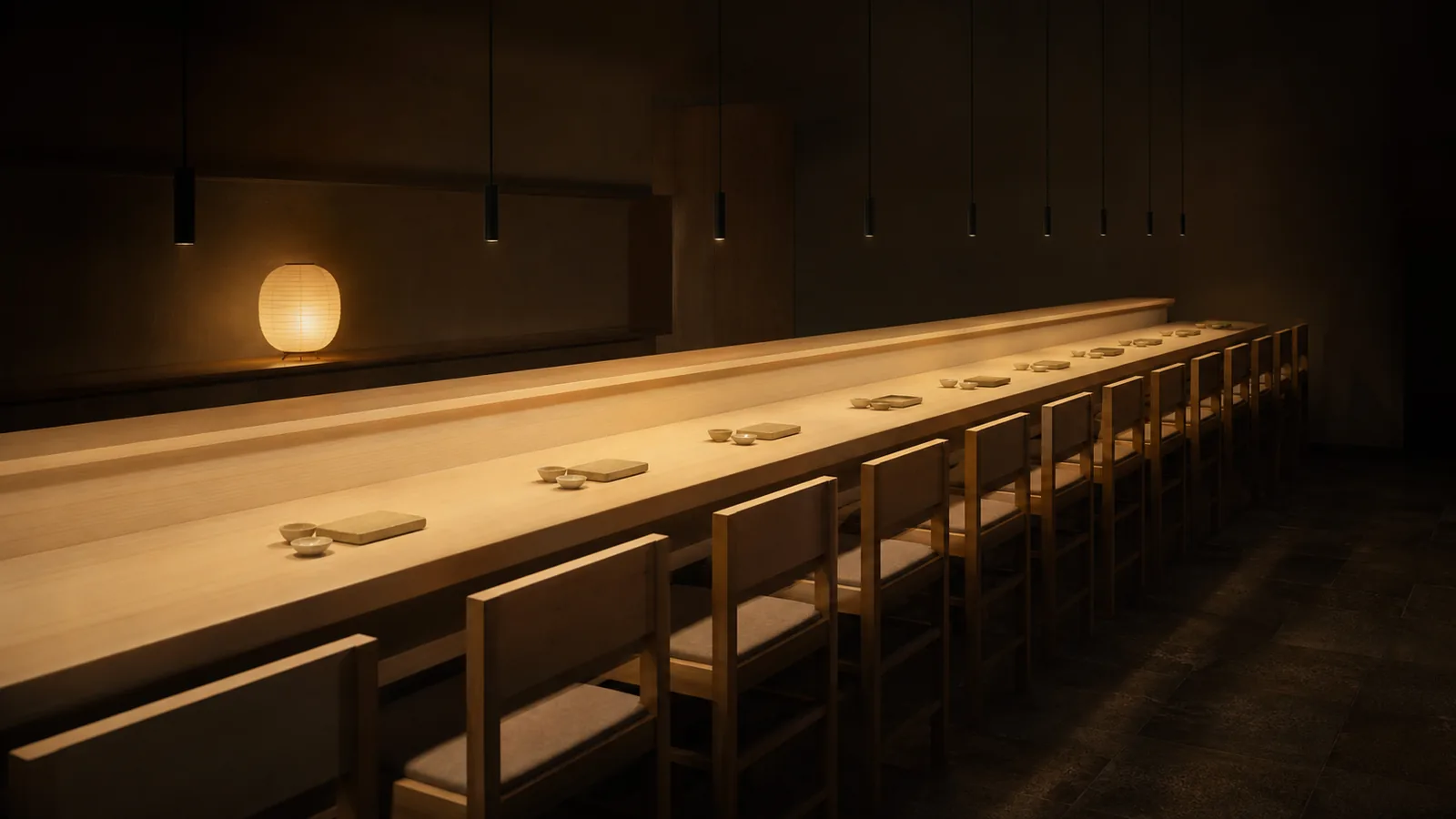 The fourteen-seat hinoki counter under warm pendant light, the room soft and dark around it