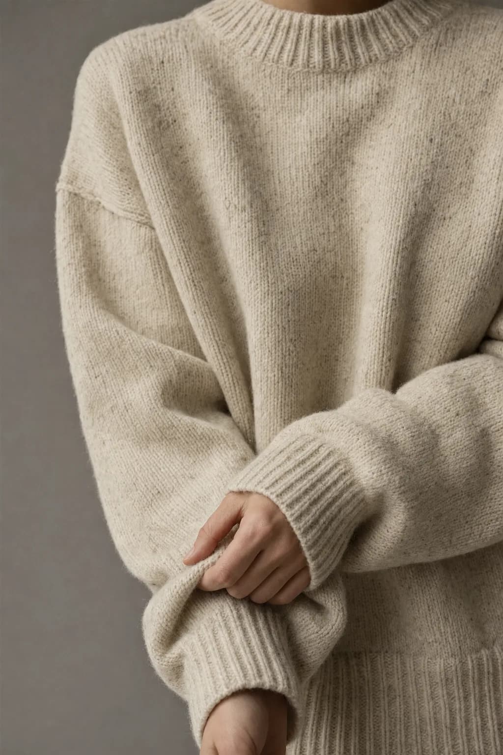 Oat recycled-wool edda knit in close crop, one hand tugging the ribbed cuff